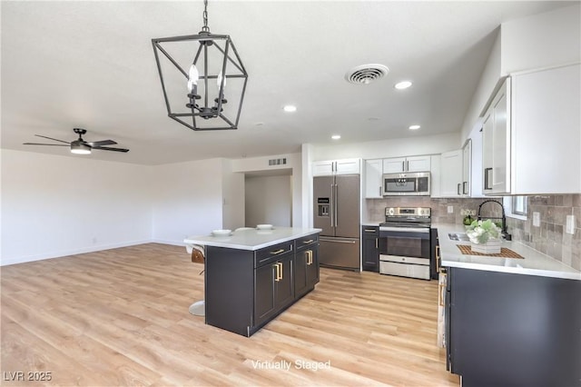 kitchen with stainless steel appliances, a kitchen island, white cabinetry, hanging light fixtures, and light countertops