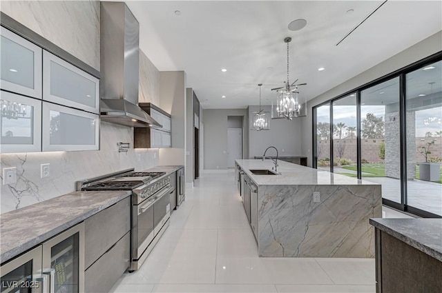 kitchen featuring wall chimney exhaust hood, sink, light stone counters, hanging light fixtures, and range with two ovens