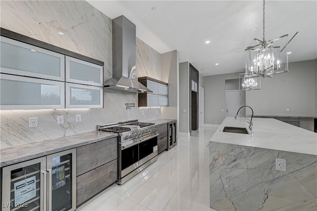 kitchen featuring sink, wine cooler, range with two ovens, light stone counters, and wall chimney exhaust hood