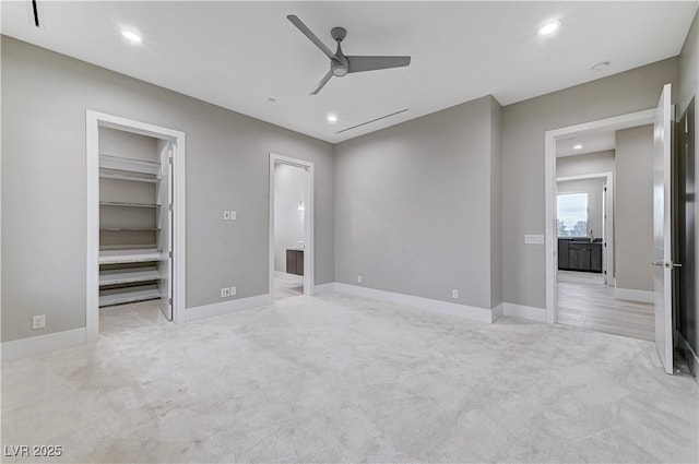 unfurnished bedroom with ceiling fan, a walk in closet, ensuite bath, and light carpet