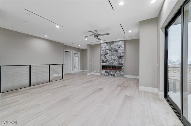 unfurnished living room featuring a large fireplace, ceiling fan, and light hardwood / wood-style flooring