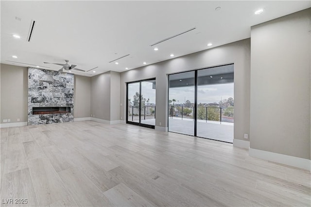 unfurnished living room with a stone fireplace, ceiling fan, and light wood-type flooring