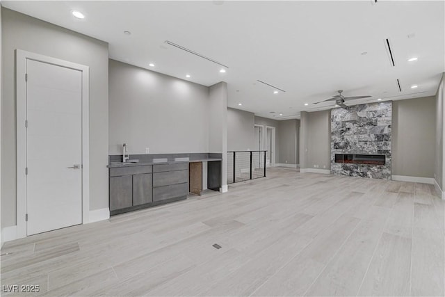 interior space with sink, a fireplace, ceiling fan, and light wood-type flooring