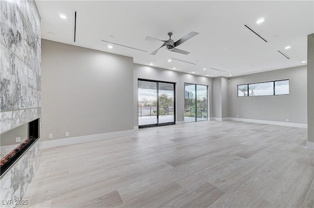 unfurnished living room with a tile fireplace, light wood-type flooring, and ceiling fan