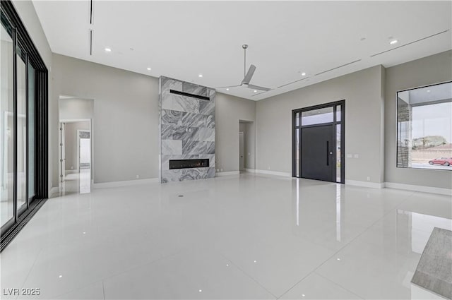 unfurnished living room with ceiling fan, a high end fireplace, light tile patterned floors, and plenty of natural light