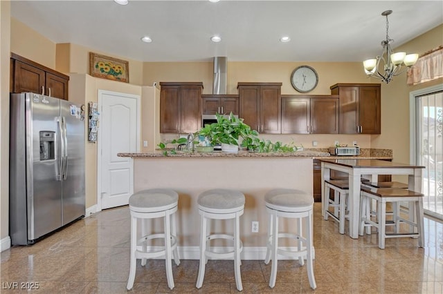 kitchen with stainless steel fridge with ice dispenser, an inviting chandelier, a kitchen breakfast bar, a center island, and baseboards