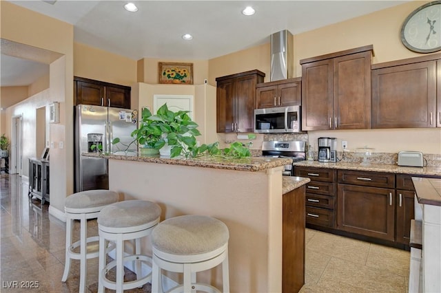 kitchen featuring a breakfast bar, recessed lighting, a kitchen island, light stone countertops, and appliances with stainless steel finishes