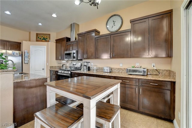 kitchen featuring a toaster, dark brown cabinets, light stone countertops, stainless steel appliances, and a sink