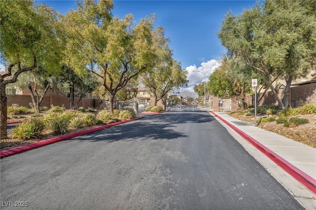 view of street featuring curbs, a gate, a gated entry, sidewalks, and street lighting