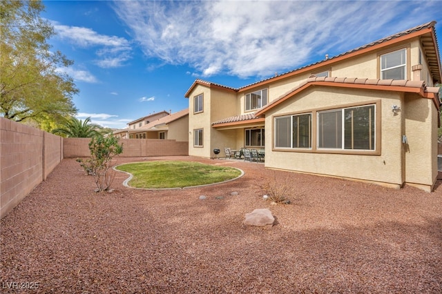 rear view of house with a tiled roof, stucco siding, a fenced backyard, and a patio area