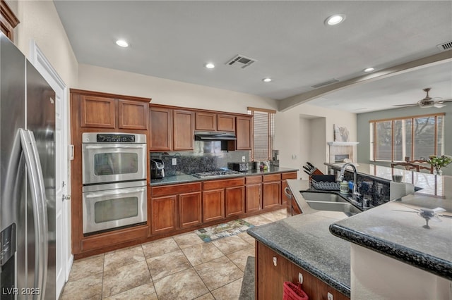 kitchen featuring visible vents, a sink, stainless steel appliances, under cabinet range hood, and a tiled fireplace