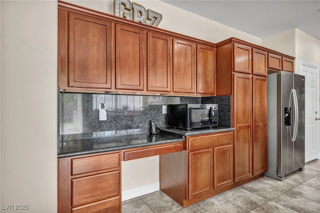 kitchen featuring stainless steel fridge, built in desk, black microwave, brown cabinets, and backsplash