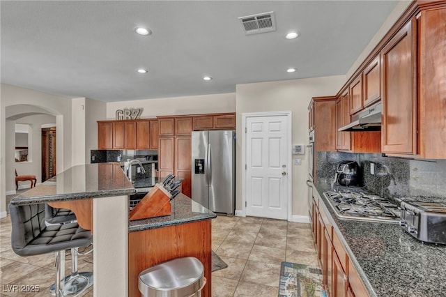 kitchen featuring tasteful backsplash, visible vents, under cabinet range hood, a breakfast bar, and appliances with stainless steel finishes