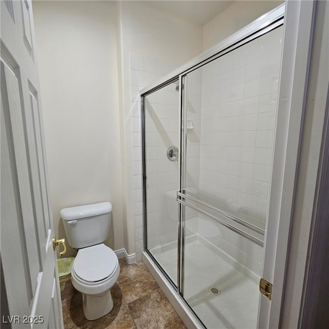 full bathroom featuring stone finish floor, a stall shower, toilet, and baseboards