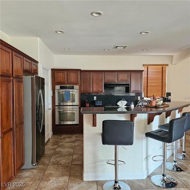 kitchen featuring visible vents, stainless steel appliances, tile patterned flooring, a kitchen breakfast bar, and tasteful backsplash