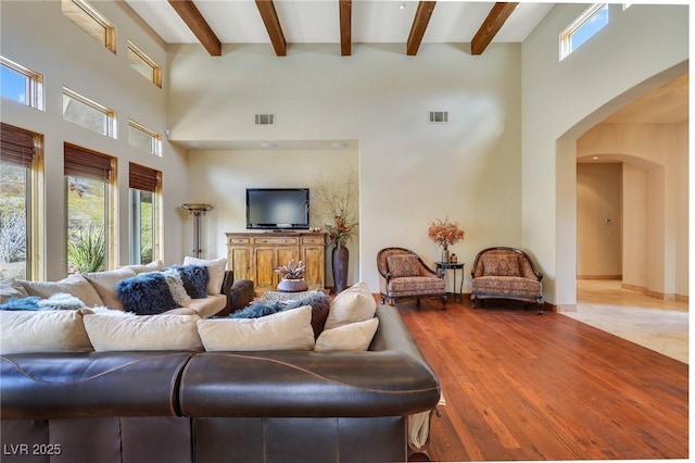 living room with arched walkways, beam ceiling, visible vents, a towering ceiling, and wood finished floors