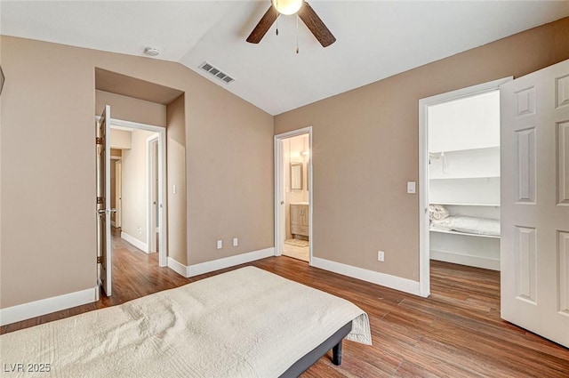 bedroom featuring lofted ceiling, connected bathroom, wood-type flooring, a walk in closet, and a closet