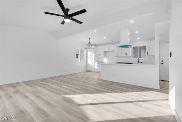 unfurnished living room with ceiling fan with notable chandelier and light hardwood / wood-style floors