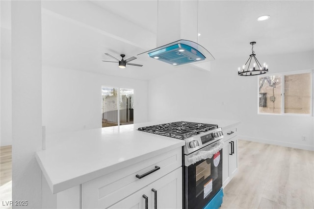 kitchen featuring stainless steel range with gas stovetop, white cabinets, ceiling fan with notable chandelier, decorative light fixtures, and light wood-type flooring