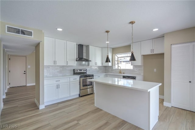 kitchen with a kitchen island, decorative light fixtures, wall chimney exhaust hood, white cabinets, and stainless steel range with electric cooktop