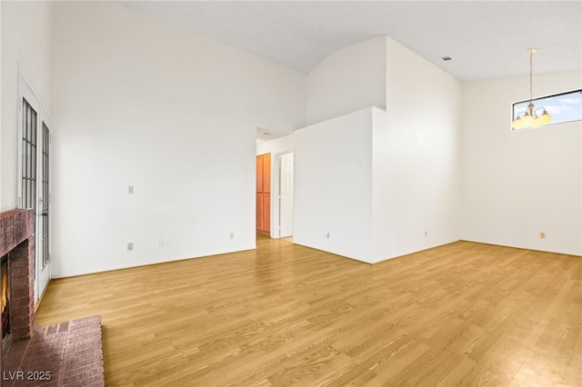 unfurnished living room with an inviting chandelier, high vaulted ceiling, a fireplace, and light hardwood / wood-style floors