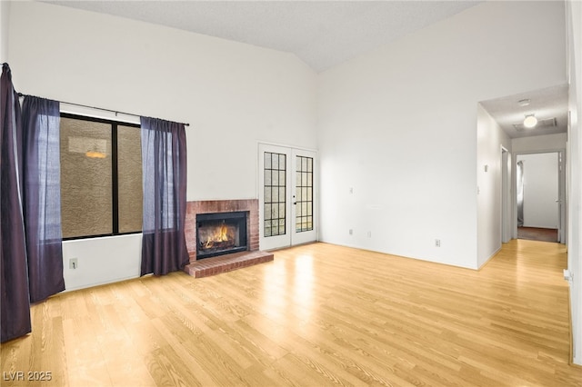 unfurnished living room with a fireplace, light hardwood / wood-style flooring, high vaulted ceiling, and french doors