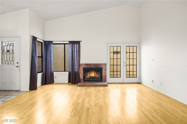 unfurnished living room featuring a brick fireplace, light hardwood / wood-style flooring, high vaulted ceiling, and french doors