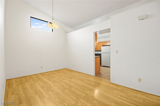 unfurnished dining area featuring vaulted ceiling, light hardwood / wood-style floors, and a textured ceiling