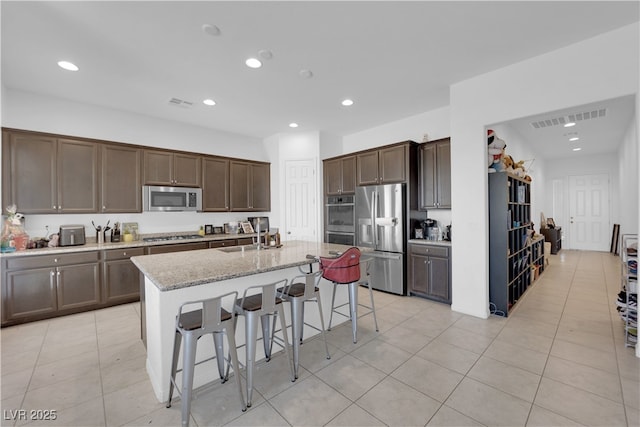 kitchen featuring sink, a breakfast bar, stainless steel appliances, light stone counters, and a center island with sink