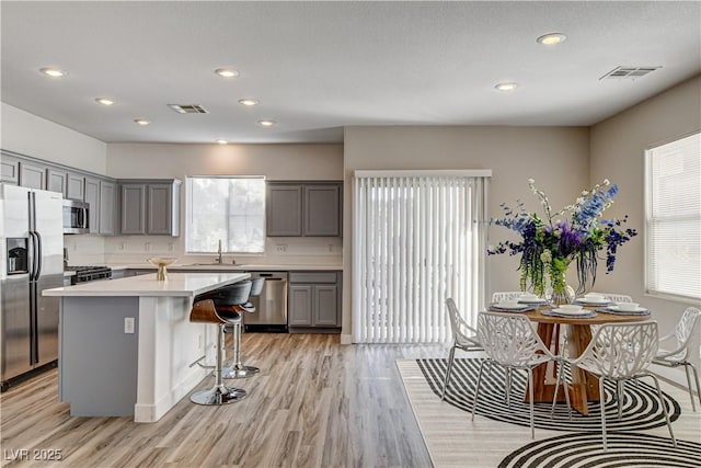 kitchen with a kitchen island, appliances with stainless steel finishes, sink, a breakfast bar area, and light wood-type flooring