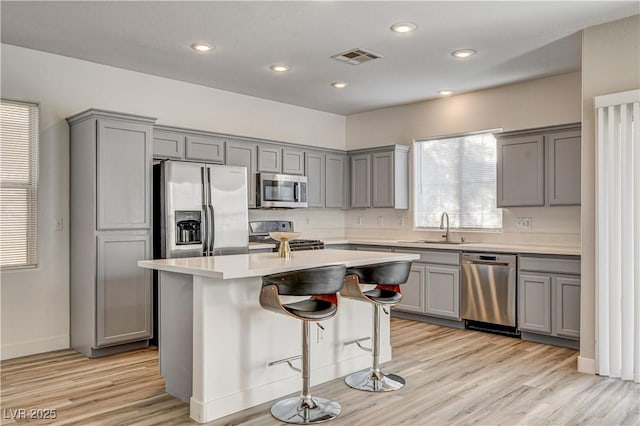 kitchen with gray cabinets, a kitchen island, a breakfast bar, sink, and stainless steel appliances