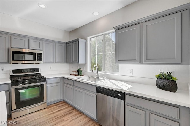 kitchen with sink, gray cabinetry, appliances with stainless steel finishes, light stone countertops, and light hardwood / wood-style floors