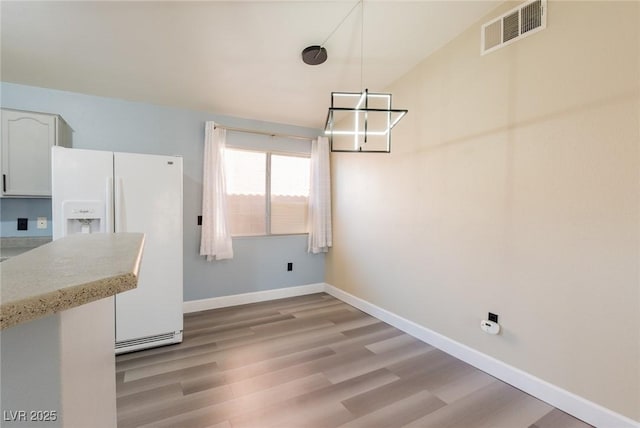 unfurnished dining area with light wood-type flooring, baseboards, visible vents, and a chandelier