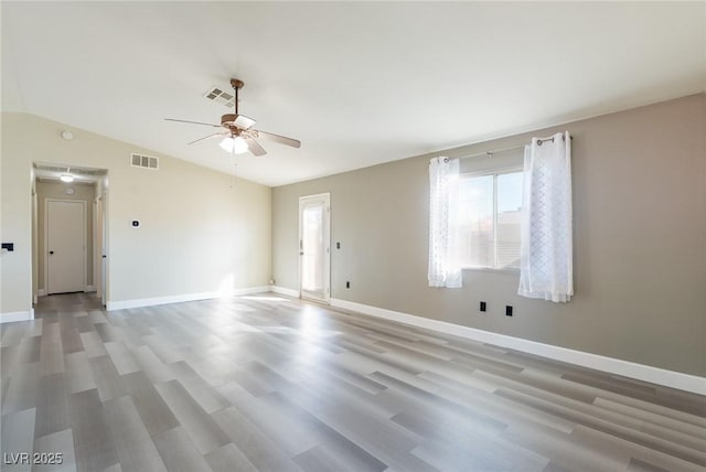 empty room with light wood-type flooring, lofted ceiling, visible vents, and baseboards