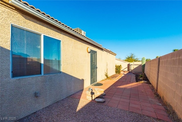 view of side of property featuring a patio area, a fenced backyard, a tile roof, and stucco siding