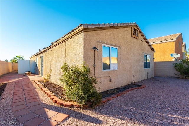 view of side of property with a tiled roof, fence, and stucco siding