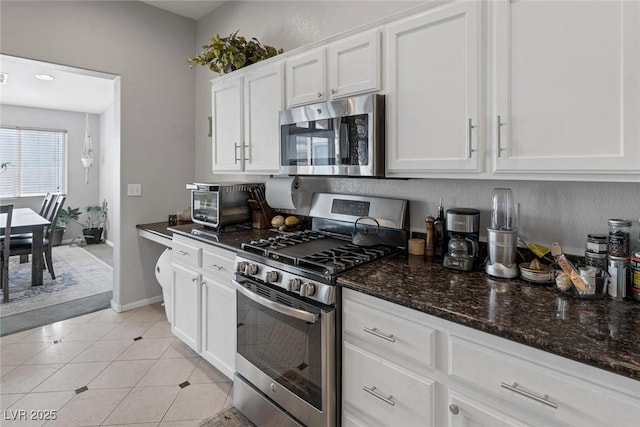 kitchen featuring dark stone countertops, stainless steel appliances, light tile patterned flooring, and white cabinets