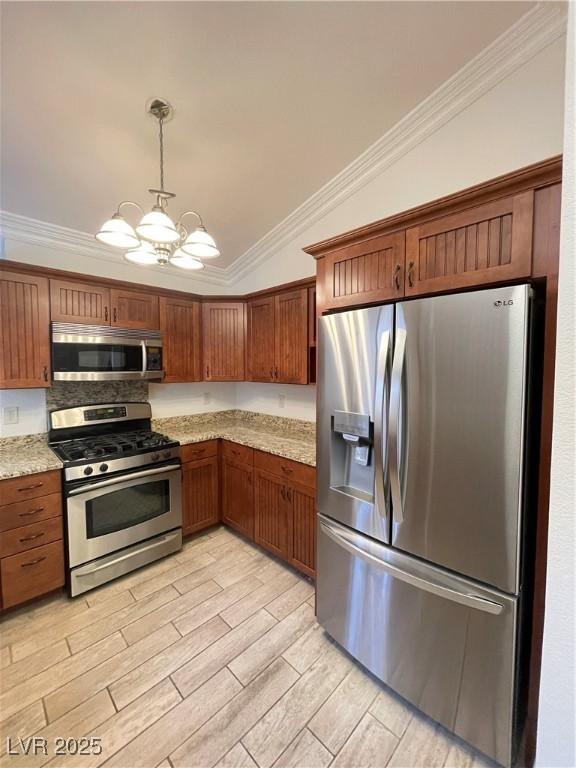 kitchen with pendant lighting, appliances with stainless steel finishes, light stone counters, ornamental molding, and vaulted ceiling