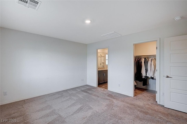 unfurnished bedroom featuring light carpet, baseboards, visible vents, and a walk in closet