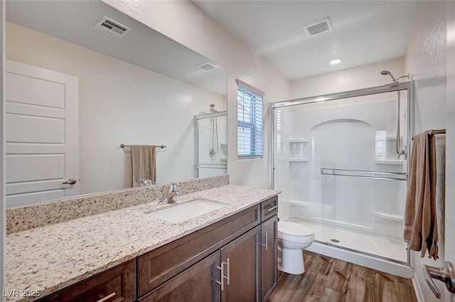 bathroom featuring toilet, a shower stall, visible vents, and wood finished floors