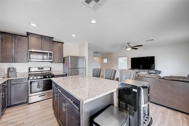 kitchen with light wood-style flooring, open floor plan, appliances with stainless steel finishes, a center island, and a kitchen bar