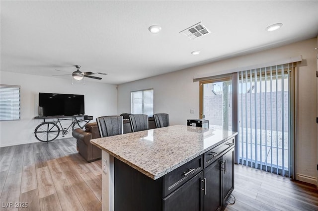 kitchen featuring light wood finished floors, visible vents, open floor plan, a center island, and light stone countertops