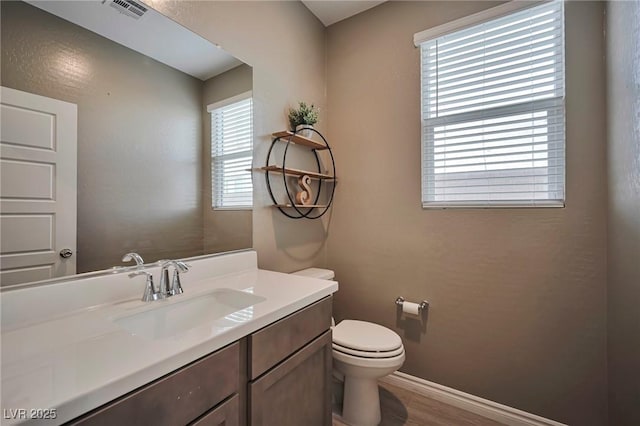 half bathroom with toilet, wood finished floors, vanity, visible vents, and baseboards