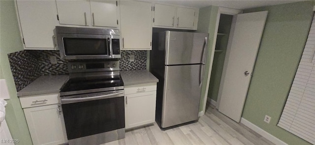 kitchen with appliances with stainless steel finishes, tasteful backsplash, white cabinets, and light hardwood / wood-style floors