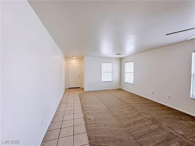 unfurnished room featuring baseboards, light colored carpet, ceiling fan, a textured ceiling, and light tile patterned flooring