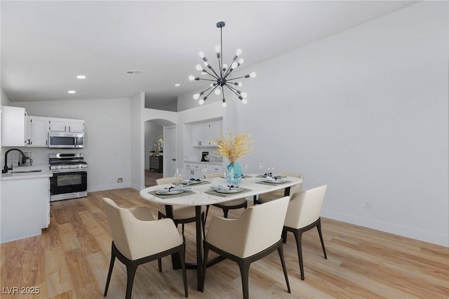 dining room featuring vaulted ceiling, sink, a notable chandelier, and light hardwood / wood-style floors