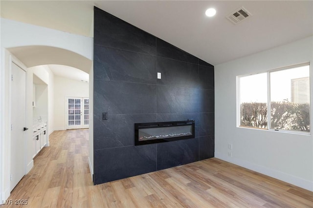 spare room with a fireplace, vaulted ceiling, and light wood-type flooring