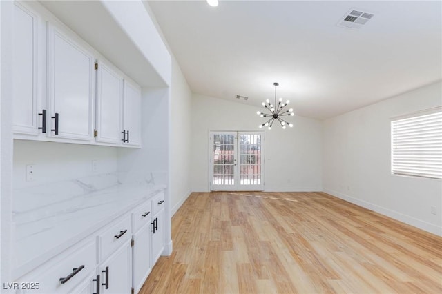 unfurnished dining area with lofted ceiling, a healthy amount of sunlight, a chandelier, and light wood-type flooring