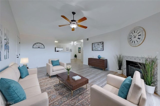 living room featuring hardwood / wood-style flooring, vaulted ceiling, a tile fireplace, and ceiling fan