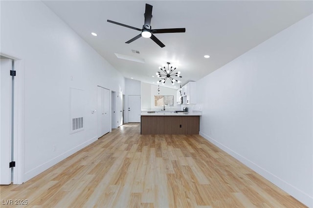 unfurnished living room with high vaulted ceiling, ceiling fan with notable chandelier, and light wood-type flooring